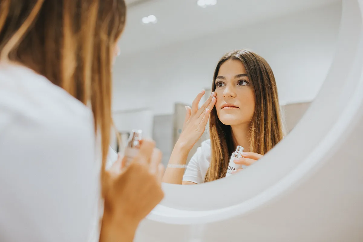 ujer aplicando un producto facial de HD Cosmetic Efficiency frente al espejo